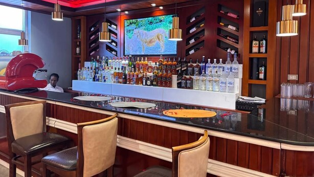 A bar with a long counter, multiple shelves of bottles, and bar stools. - 2RN Solomon Hotel (Sendafa)