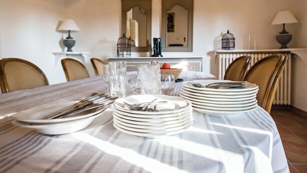 Una mesa de comedor dispuesta con platos, cubiertos y vasos, rodeada de sillas.
