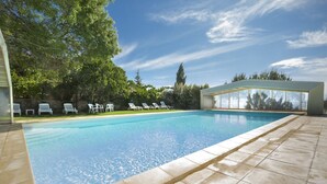 Una piscina con sillas de descanso, una zona cubierta y vistas a árboles y al cielo.