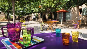 Una mesa con bebidas coloridas y una jarrón, ubicada al aire libre con árboles y un edificio al fondo.