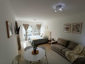 A hotel room with a bed, a sofa, a table with chairs, a small plant, and artwork on the walls. - Beautiful Studio Apartment in Green Park II, Solanas (Maldonado)