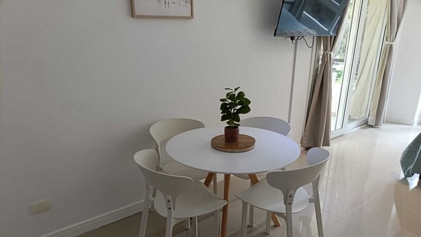 A dining area with a round table, white chairs, a potted plant, and a TV mounted on the wall. - Beautiful Studio Apartment in Green Park II, Solanas (Maldonado)