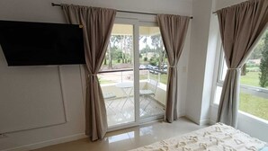 A room with a bed, a flat-screen TV mounted on the wall, and a sliding glass door leading to an outdoor patio. - Beautiful Studio Apartment in Green Park II, Solanas (Maldonado)