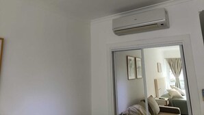 A hotel room with a sliding door leading to a balcony, a bed with pillows, a bedside table, and a wall-mounted air conditioning unit. - Beautiful Studio Apartment in Green Park II, Solanas (Maldonado)