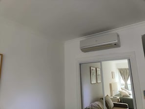 Ein Hotelzimmer mit einer Schiebetür, die auf einen Balkon führt, einem Bett mit Kissen, einem Nachttisch und einer wandmontierten Klimaanlage.
