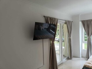 Ein Zimmer mit Wandfernseher, einer Schiebeglastür und Vorhängen.