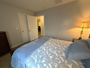 A bedroom with a bed, a dresser, a lamp, and a door leading to another room.