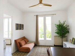 Ein Zimmer mit braunem Sofa, Deckenventilator, Pflanze und einem Fenster mit Vorhängen.