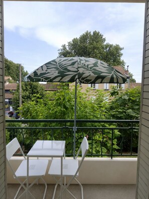 Ein Balkon mit Tisch und Stühlen, einem gemusterten Sonnenschirm und Blick auf Häuser und Bäume.