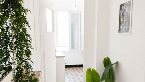 A hallway with a tiled floor, a plant on the right, and a door leading to another room. - Cozy & bright 2-bedroom apartment - Avignon - 700 m from the city walls (Avignon)