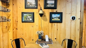 A wooden-paneled wall with four framed photographs, a table with chairs, a lamp, and a small plant. - Cozy cabin in Davis, WV 
Hibernation Station - Black Bear Resort (Davis)