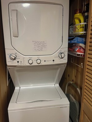 A front view of a white washing machine with a control panel, a step stool, and a shelf with laundry supplies. - Cozy cabin in Davis, WV 
Hibernation Station - Black Bear Resort (Davis)