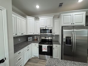 A modern kitchen with white cabinetry, stainless steel appliances, granite countertops, and a black oven with a towel hanging on it. - 3-bedroom house in Ruston near LA Tech & Ruston Sports Complex (Ruston)