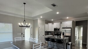 A modern kitchen with white cabinets, a central island with bar stools, a stainless steel refrigerator, and a dining area with a table and chairs. - 3-bedroom house in Ruston near LA Tech & Ruston Sports Complex (Ruston)