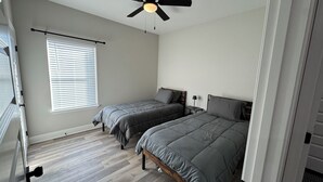 A bedroom with two beds, a ceiling fan, a window with blinds, and a wooden floor. - 3-bedroom house in Ruston near LA Tech & Ruston Sports Complex (Ruston)