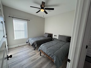Ein Schlafzimmer mit zwei Betten, einem Deckenventilator, einem Fenster mit Jalousien und Holzboden.
