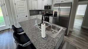 A modern kitchen with white cabinetry, granite countertops, stainless steel appliances, and a black chair. - 3-bedroom house in Ruston near LA Tech & Ruston Sports Complex (Ruston)