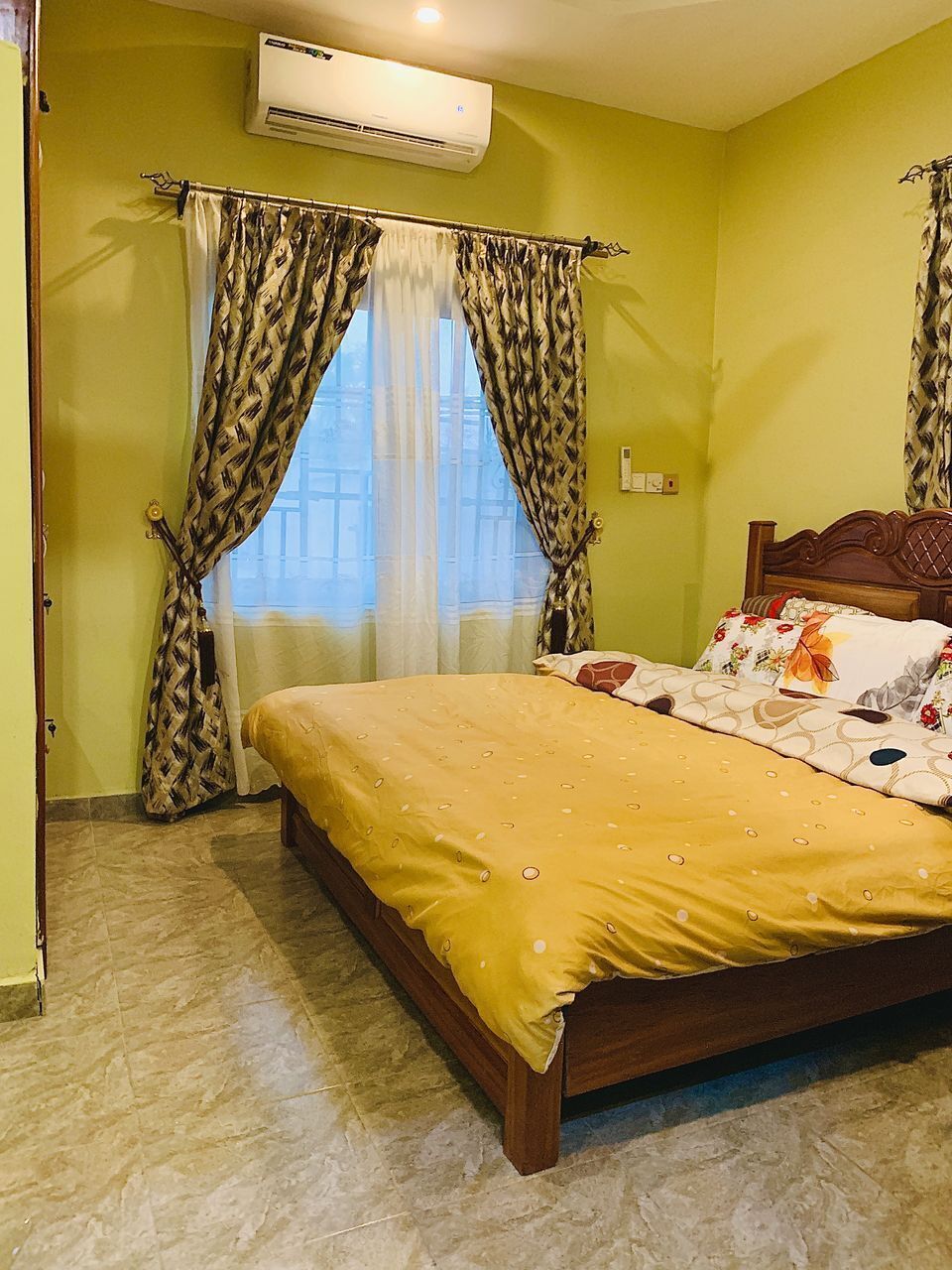 A bedroom with a bed, curtains, an air conditioner, and a window.