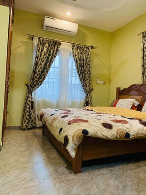Une chambre à coucher avec un lit, des rideaux, un appareil de climatisation et un sol carrelé.