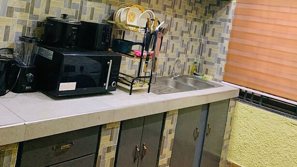 Een keuken met grijze kastjes, een betegelde spatwand en een aanrecht met een koffiezetapparaat en een afwasschaal.