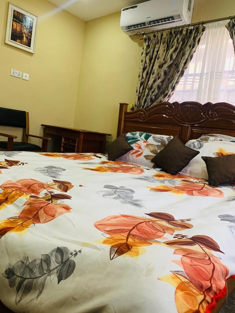 Une chambre d’hôtel avec un lit, une tête de lit, un climatiseur fixé au mur, un tableau encadré et une fenêtre avec des rideaux.