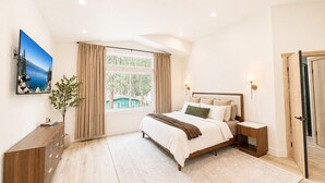 A bedroom with a bed, bedside tables, a nightstand, a window with curtains, a radiator, a wall-mounted TV, and a door. - South Lake Tahoe Home Near Heavenly, Edgewood Golf & beaches (SLT1040) (South Lake Tahoe)