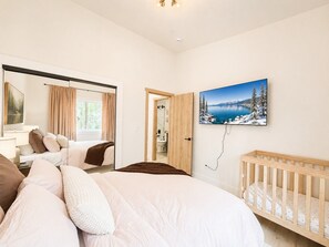 A bedroom with a bed, a crib, a painting of a snowy landscape, and a bathroom visible through a door.