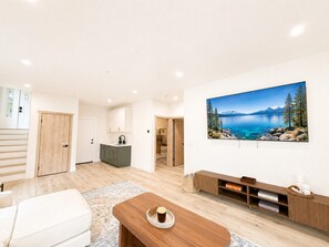 A modern living room with a large window, a wooden coffee table, a sofa, and a painting of a lake.