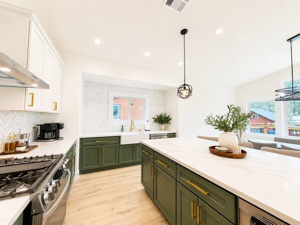 A modern kitchen with a large island, green cabinets, and a herringbone-patterned backsplash.