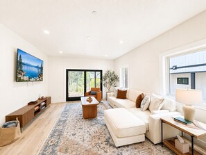 A modern living room with a large flat-screen TV, a sofa, a coffee table, and a patterned rug.
