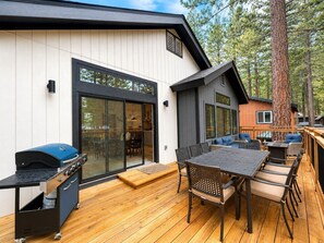 A deck with a barbecue, dining area, and a large window overlooking a forest.
