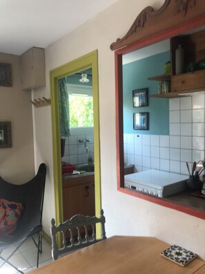 A dining area with a wooden table, a chair with a floral pattern, a mirror, and a kitchen visible through an open doorway. - Lovely 1-bedroom house in Saint-Nazaire near the coast (Saint-Nazaire)