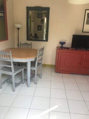 A dining table with chairs, a mirror, a television, and a red cabinet in a room with tiled flooring. - Lovely 1-bedroom house in Saint-Nazaire near the coast (Saint-Nazaire)