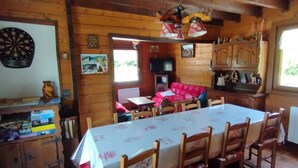 Un intérieur en bois avec un jeu de fléchettes, une table avec des chaises, un canapé rouge et un téléviseur.