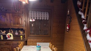 Un espace repas avec une longue table recouverte d’une nappe à motifs rouges, entourée de chaises en bois.