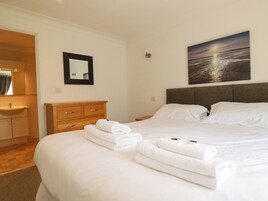 A hotel room with a bed, a nightstand, a dresser, a mirror, and a painting of a sunset over water.