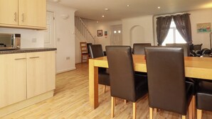 Un comedor con una mesa y sillas de madera, una cocina con armarios de madera, y una escalera que lleva a otro nivel.
