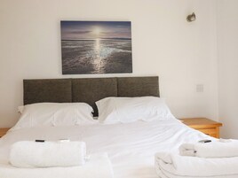 A neatly made bed with white linens, a headboard, and two bedside tables with towels.