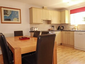 A compact kitchen with wooden cabinets, a dining table with chairs, and a dishwasher. - 62 Golf Lodges (St. Columb Major)