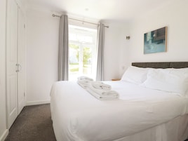 A hotel room with a bed, a door, a window with curtains, and a painting on the wall.