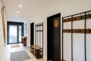 A modern hallway with a wooden bench, a coat rack, and a door with a number plaque. - Suite Myrtilles - Bel appartement moderne pour 4 (Saint-Chaffrey)
