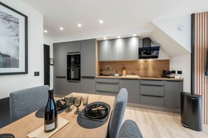 A modern kitchen with grey cabinets, a wooden countertop, and a dining area with a table set for two. - Suite Myrtilles - Bel appartement moderne pour 4 (Saint-Chaffrey)