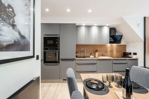 A modern kitchen with grey cabinetry, a wooden countertop, and a dining area with a table set for two. - Suite Myrtilles - Bel appartement moderne pour 4 (Saint-Chaffrey)