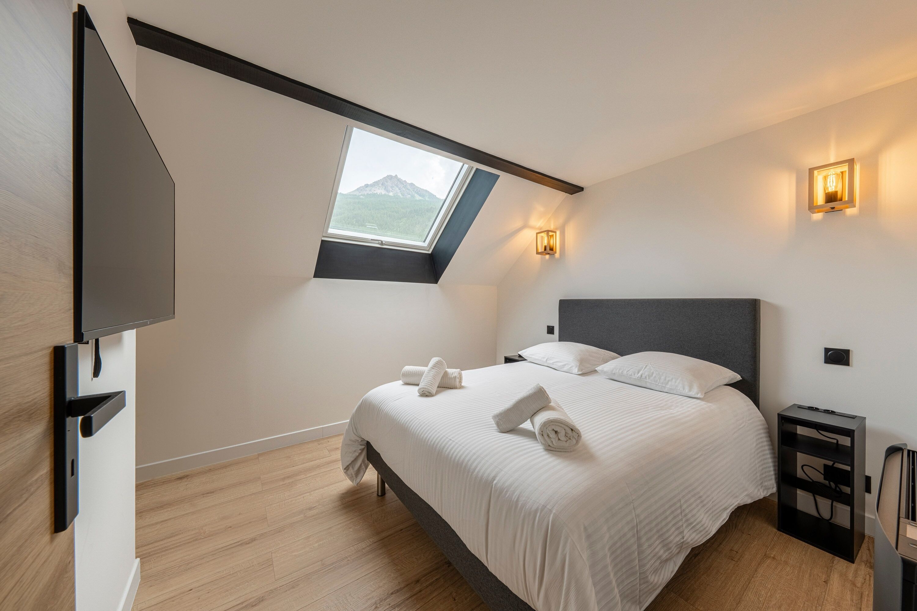 Un dormitorio con cama, tragaluz, televisor y mesita de noche.