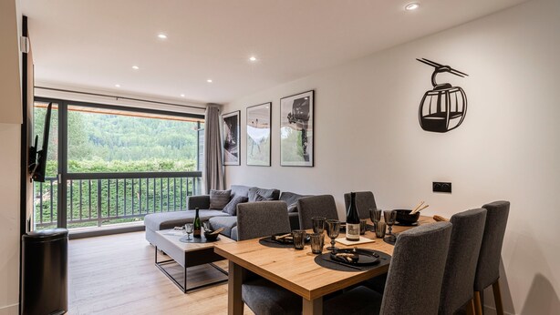 En moderne spiseplads med et træbord, grå polstrede stole og en balkon med et smukt udsyn.