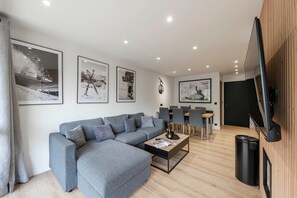 Een moderne woonkamer met een grijze modulaire bank, een salontafel en een televisie bevestigd aan een houten wand.