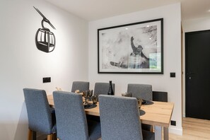 Een moderne eetruimte met een houten tafel, gestoffeerde grijze stoelen, een lijstwerk abstract kunstwerk en een zwarte deur.