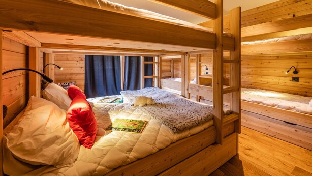 Camera con letto a castello, pareti in legno, un letto singolo con copriletto e cuscini, un comodino e una lampada.
