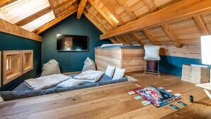 Una camera mansardata accogliente con soffitto spiovente, un letto con cuscini, una TV a muro e un piccolo tavolo con giochi da tavolo.