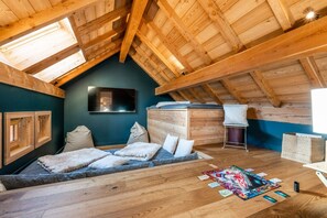 A cozy attic room with a sloped ceiling, a bed with pillows, a mounted TV, and a small table with board games. - Malago - Five Bedroom Chalet, Sleeps 14 (Le Monêtier-les-Bains)